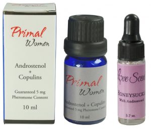 Two products sit next to each other: Primal Women, with a blue bottle and gray label with red and black text and a white box with red and black text, and Love Scent Honeysuckle oil, with a clear eyedropper bottle and purplish-pink label with black text.