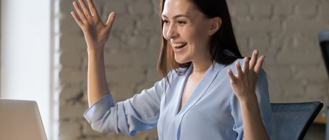 A woman in an office raises her hands happily at her computer