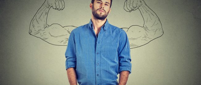 A man in a denim shirt stands with his hands in his pockets. Two illustrated arms are showing off strong mucles behind him, making it look like the arms are growing out of his shoulders.