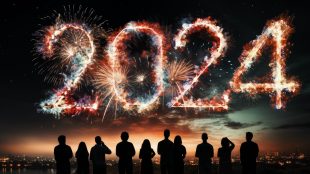 A group of people look up at fireworks in the night sky. The fireworks are spelling out the number 2024 to welcome the new year.