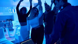 A group of adults dancing with their hands in the air at a house party.