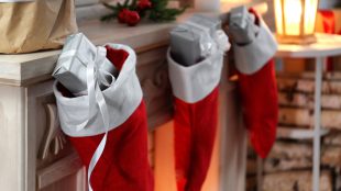 A row of Christmas stockings on a mantelpiece with small, silver-wrapped gifts sticking out of their tops.
