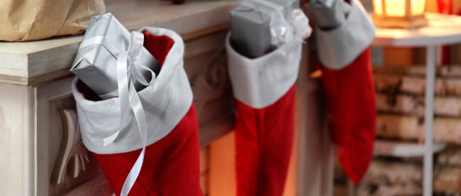 A row of Christmas stockings on a mantelpiece with small, silver-wrapped gifts sticking out of their tops.