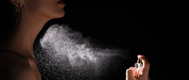 A woman sprays perfume onto her neck.