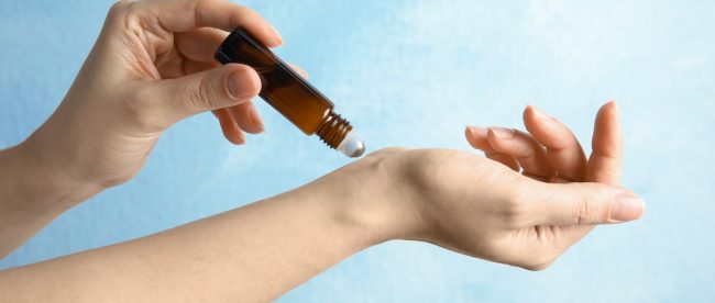 Close up view of a woman's hands as she uses a brown roller-ball bottle to apply pheromones to her wrist.