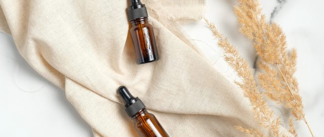Two brown eyedropper bottles sit on a brown cloth in the sunlight.